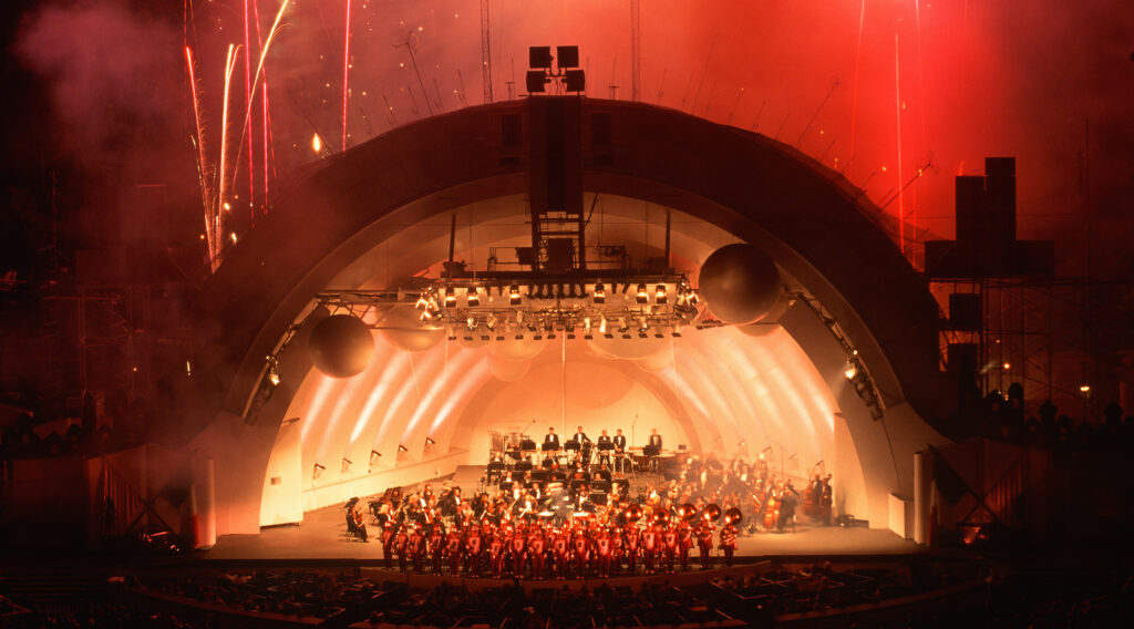 Hollywood Bowl at night with a marching band and orchestra with fireworks in the background
